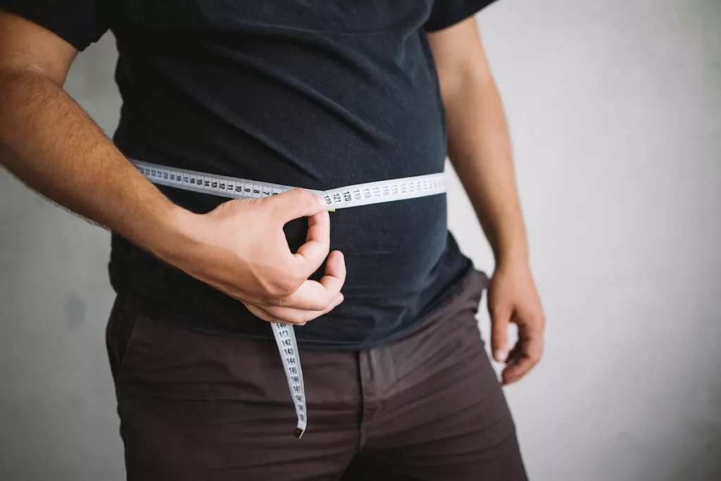 Overweight man measuring waist with measure tape